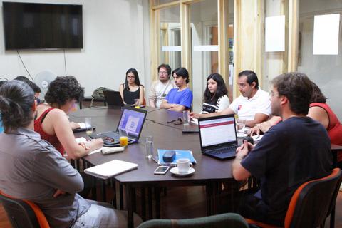 Reunión de trabajo en una sala con varias personas sentadas alrededor de una mesa.