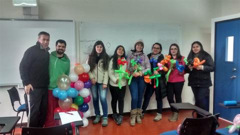 Un grupo de seis personas sonrientes sostiene globos de diferentes formas en un aula.