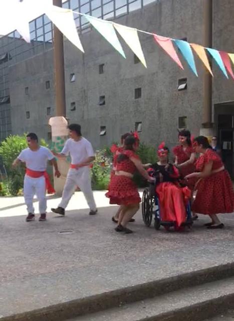 Grupo de personas bailando en un escenario al aire libre, con trajes rojos y decoraciones coloridas.