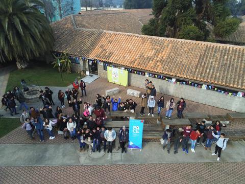 Un grupo de estudiantes sonrientes se reúne al aire libre frente a un edificio con un tejado de tejas.