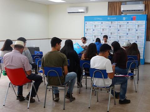 Un grupo de personas sentadas en sillas en un salón, observando un evento o reunión.
