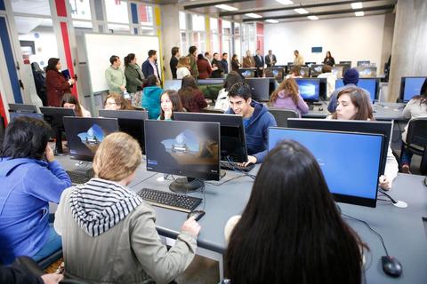 Una sala llena de estudiantes trabajando en computadoras mientras otros esperan en fila.