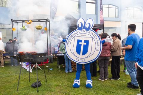 Una feria con un personaje disfrazado y parrillas al aire libre, donde se pueden ver personas disfrutando de la comida.
