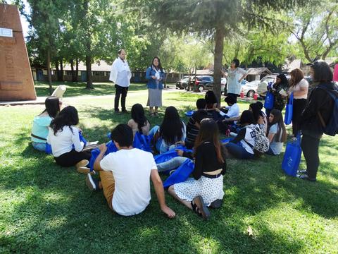 Un grupo de personas jóvenes escucha atentamente a dos oradores en un parque.