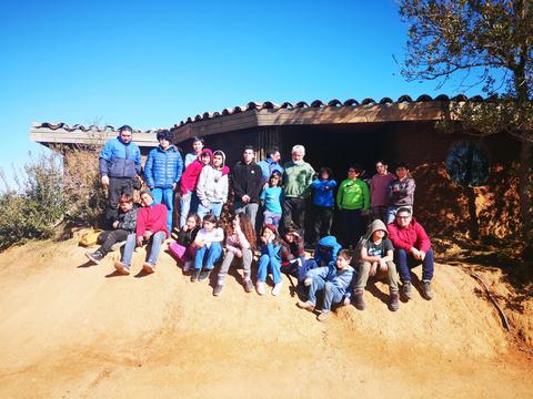 Un grupo de jóvenes y adultos posando en un entorno al aire libre frente a una construcción de barro.