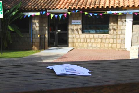 La imagen muestra un edificio con un techo de tejas y un tablón de madera en primer plano, junto a algunos folletos sobre la mesa.