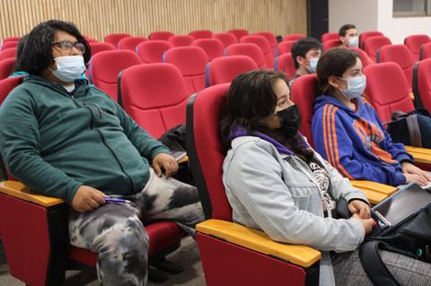 Un grupo de jóvenes sentados en un aula, usando mascarillas y escuchando atentamente.