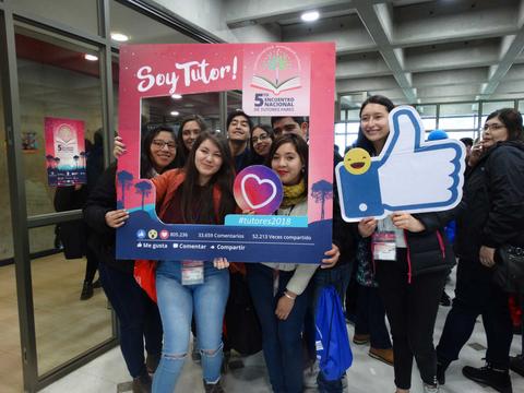 Un grupo de jóvenes sonrientes sostiene un marco que dice 'Soy Tutor!' en un evento.