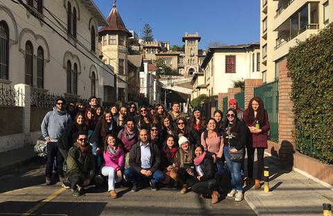 Un grupo grande de personas posando en una calle con edificios y un cielo despejado de fondo.