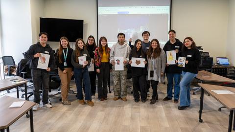 Un grupo de jóvenes en un salón mostrando dibujos y sonriendo.