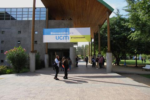 Un grupo de estudiantes entra a un campus universitario bajo un cartel de bienvenida.