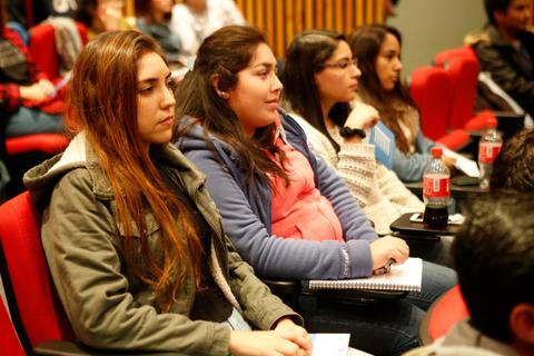 Un grupo de jóvenes atentos en un evento, sentados en sillas rojas.