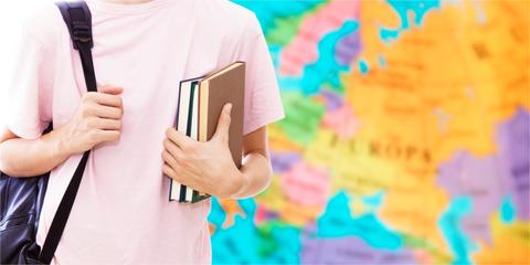 Un estudiante sostiene libros frente a un mapa colorido de Europa.