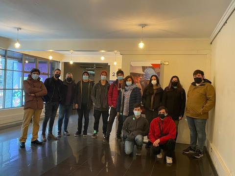 Un grupo de personas, todas con mascarillas, posando dentro de un edificio con paredes claras y iluminación suave.