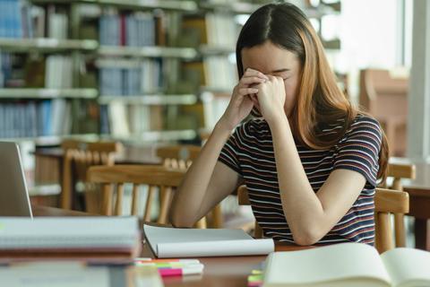 Una joven estresada se cubre la cara con las manos mientras estudia en una biblioteca.