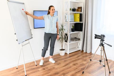 Una mujer está presentando frente a un proyector mientras sostiene un marcador y señala una pizarra blanca.