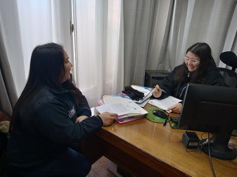 Dos mujeres conversando en una oficina sobre documentos en un escritorio.