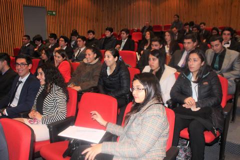 Un grupo de estudiantes sentados en un auditorio con asientos rojos, escuchando atentamente.