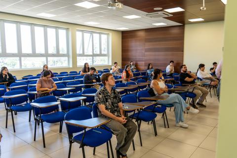 Una sala de clases con muchos estudiantes sentados en sus pupitres esperando la clase.