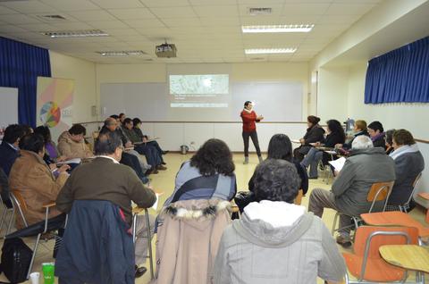 Una reunión en un aula con un presentador hablando frente a un grupo de personas sentadas.