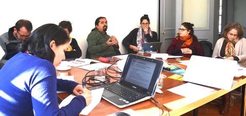 Un grupo de personas se encuentra en una reunión alrededor de una mesa con computadoras y papeles.