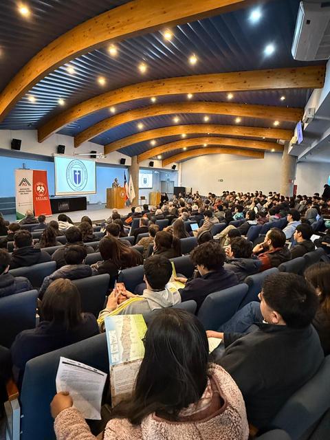 Una multitud de estudiantes asiste a una charla en un auditorio con un diseño moderno.