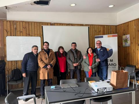 Un grupo de seis personas posando frente a una pantalla en un entorno de reunión.