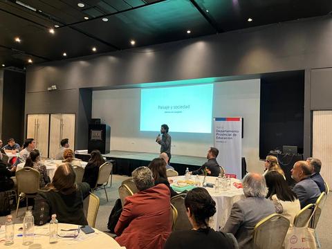 Un conferencista presenta sobre el tema 'Paisaje y sociedad' ante un público atento en un evento.