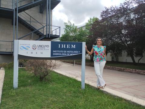 Una mujer sonriente posa junto a un letrero del Instituto de Histología y Embriología de Mendoza.