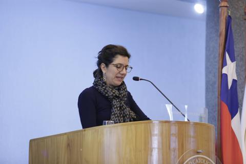 Una mujer habla en un micrófono frente a un podio de madera en un evento formal.