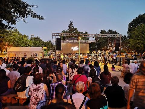 Una multitud disfruta de un concierto al aire libre en un parque al atardecer.