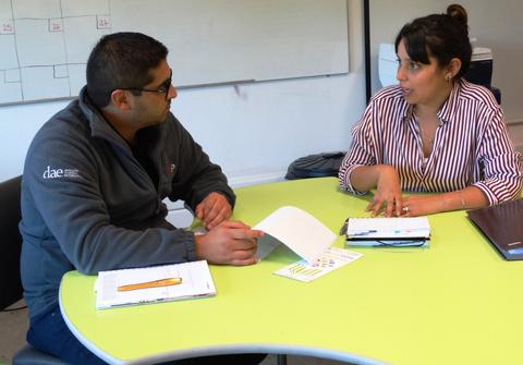 Dos personas están conversando en una mesa con documentos y material de escritura.