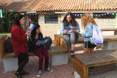 Cuatro mujeres revisan folletos sentadas en bancos de una plaza al aire libre.