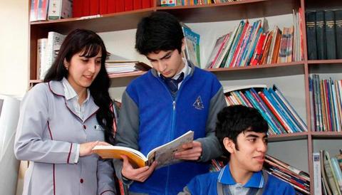 Un grupo de estudiantes y una profesora revisan un libro en una biblioteca escolar.