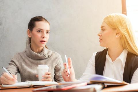 Dos mujeres conversando durante una reunión en un ambiente de trabajo.