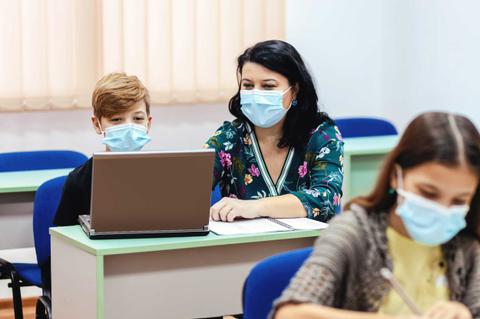 Una mujer y un niño usan mascarillas mientras trabajan en un ordenador portátil en un aula.