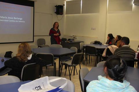 Una profesora da una charla en un aula con varios estudiantes escuchando atentamente.