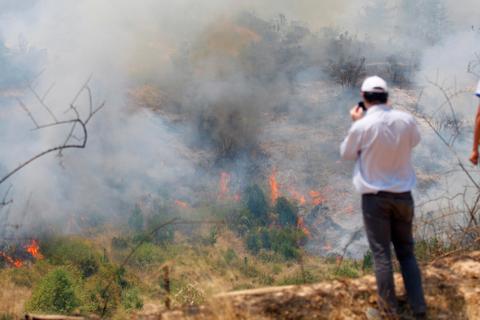 Un hombre observa un incendio forestal mientras el humo y las llamas se propagan en la vegetación.