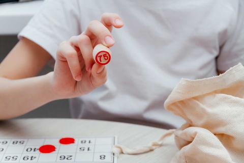 Un niño sostiene un fichaje de bingo con el número 75, mientras descansa sobre una mesa con un cartón de bingo y fichas rojas.