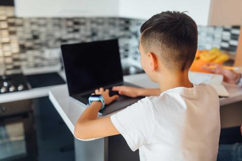 Un niño sentado frente a un computador portátil en una cocina moderna.
