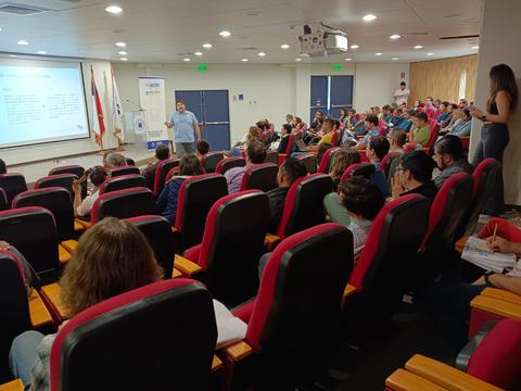 Imagen de un evento con muchas personas sentadas escuchando a un ponente en un auditorio.