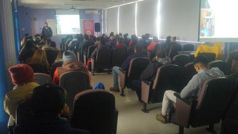 Un grupo de personas asistiendo a una charla en un salón con asientos en fila.