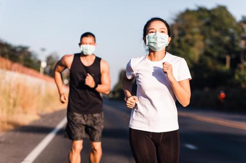 Un hombre y una mujer corren por una carretera, ambos usando mascarillas.