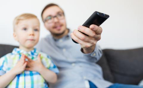 Un hombre y un niño están viendo la televisión mientras el hombre sostiene el control remoto.