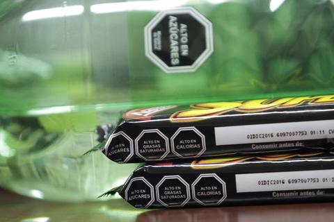 En la imagen se muestra una botella de agua junto a dos paquetes de un producto alimenticio con etiquetas que indican su contenido nutricional.