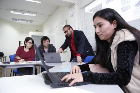 Grupo de estudiantes trabajando en una clase colaborativa con laptops.
