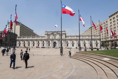 Una vista de la Plaza de La Moneda en Santiago de Chile con varias banderas ondeando y personas caminando.