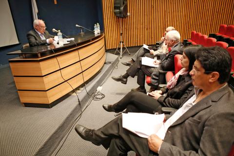 Un panel de discusión con un orador frente a una audiencia en una sala con sillas rojas.