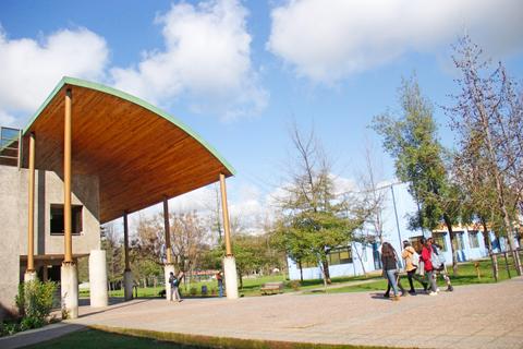 La imagen muestra un edificio moderno con un diseño arquitectónico distintivo, rodeado de árboles y un cielo despejado.