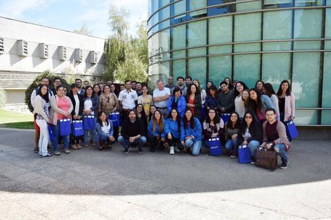 Un grupo grande de personas posando frente a un edificio moderno envueltas en un ambiente alegre.
